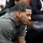 Wander Franco condenado a tres años de prisión suspendida por abuso Wander Franco, con camisa verde oliva y un tatuaje en el cuello, sentado de perfil en un banco de madera de una sala de audiencias