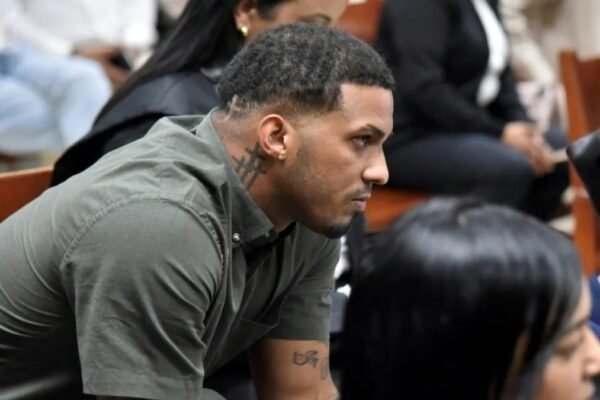 Wander Franco, con camisa verde oliva y un tatuaje en el cuello, sentado de perfil en un banco de madera de una sala de audiencias