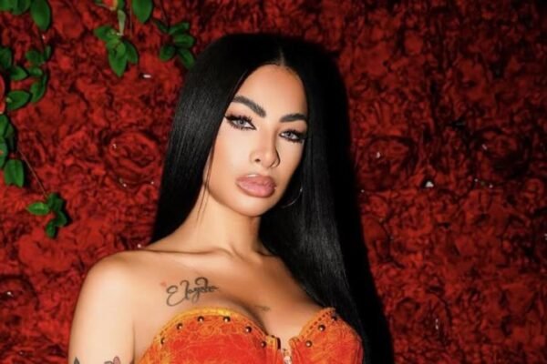 Retrato de la artista Yailin La Más Viral, con el cabello largo y negro y un corpiño naranja, ante un fondo de rosas rojas