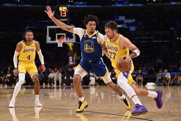 Un jugador de los Warriors defiende a un jugador de los Lakers con el número 77, que bota el balón en una cancha de la NBA