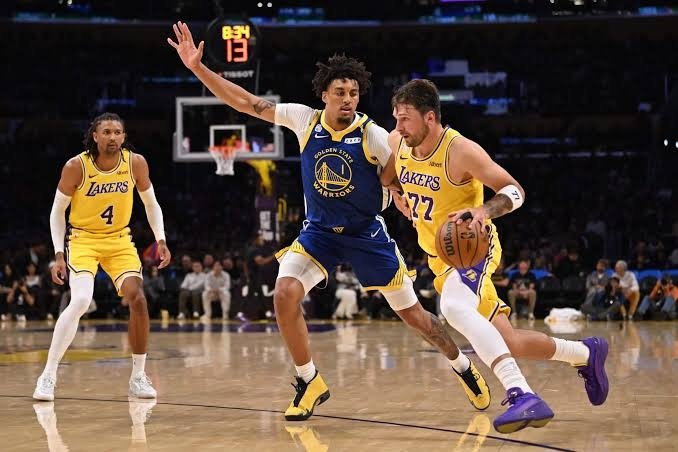 Un jugador de los Warriors defiende a un jugador de los Lakers con el número 77, que bota el balón en una cancha de la NBA