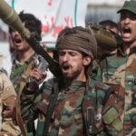 Combatientes yemeníes armados, uno con un lanzacohetes al hombro, corean consignas durante una concentración