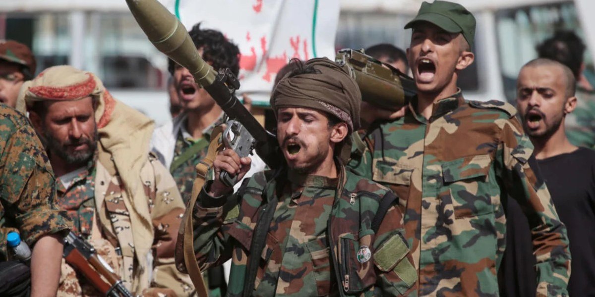Combatientes yemeníes armados, uno con un lanzacohetes al hombro, corean consignas durante una concentración