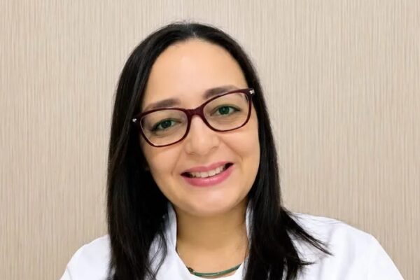 Ylsa Quero Cabrera, con gafas y bata blanca, sonríe ante una pared beige